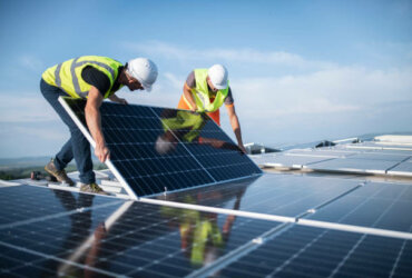 Team of two engineers installing solar panels on roof.